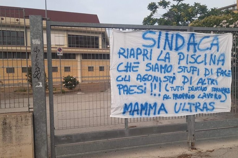 Lo striscione affisso al cancello della piscina comunale